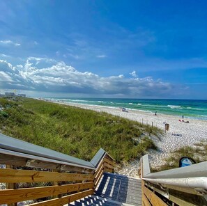 Ein Strand mit einer Holzpromenade, die zum Ufer führt, unter klarem Himmel und mit sanften Wellen.