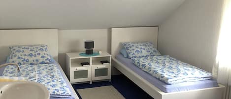 A bedroom with two beds, a nightstand, a bedside table, a window, and a bathroom with a sink.