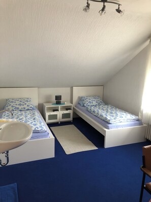 A bedroom with two beds, a nightstand, a bedside table, a window, and a bathroom with a sink.