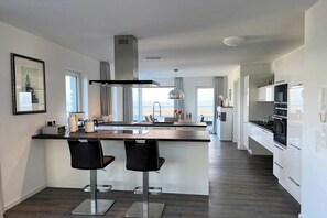 A modern kitchen with a central island, bar stools, and a view to the outside. - Holiday apartment with 1 bedroom (Wangerland)