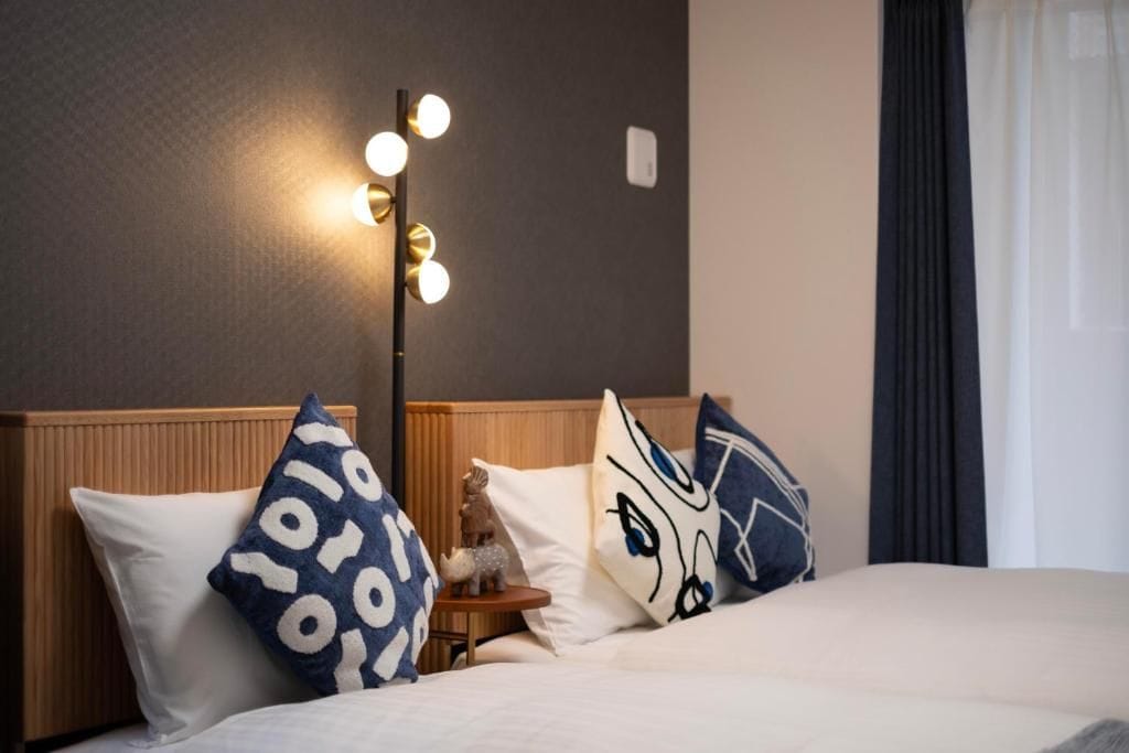 Une chambre d’hôtel comprenant un lit, des oreillers, une table de chevet, une lampe et un luminaire fixé au mur.