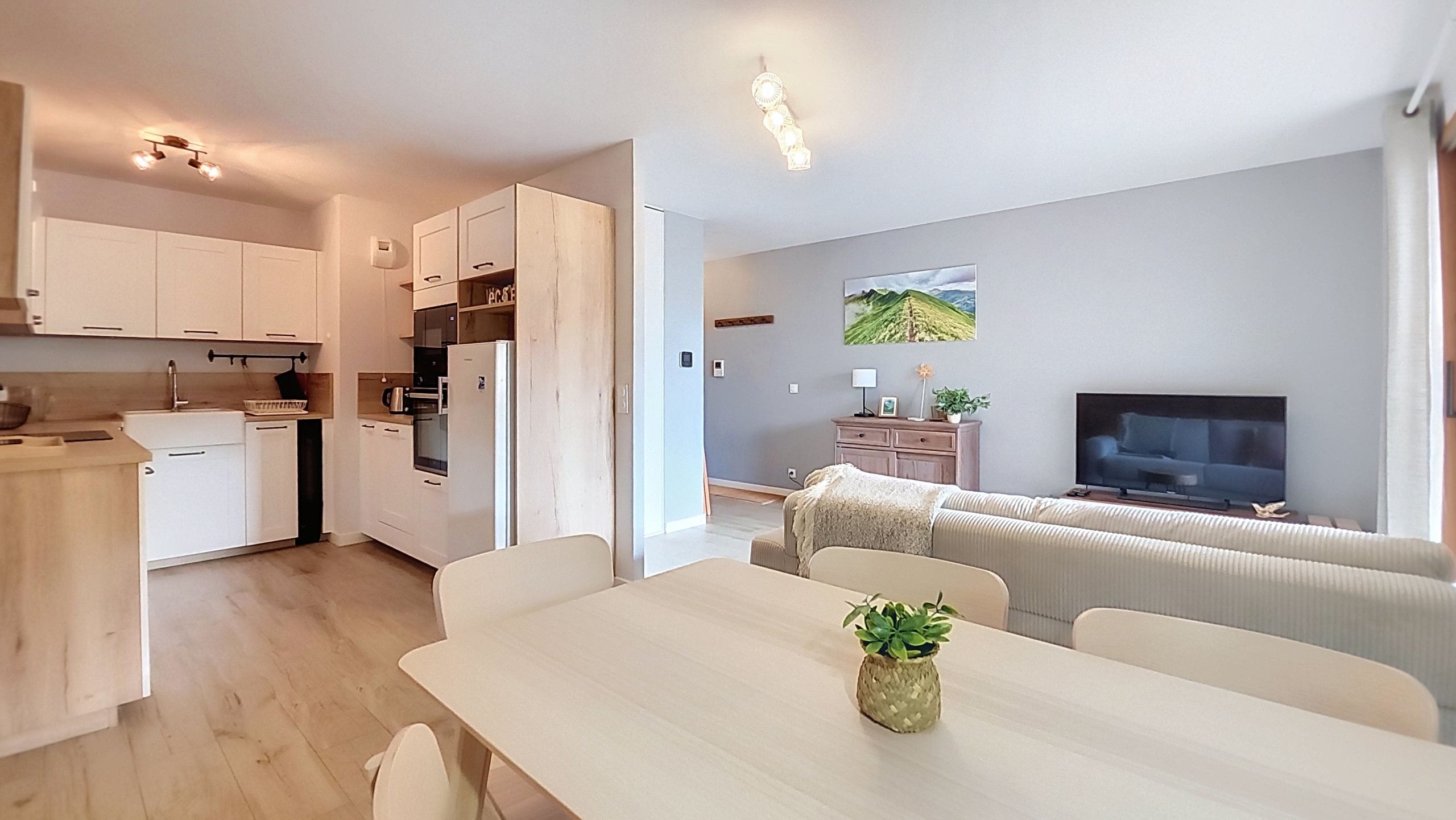 A modern kitchen with white cabinets, a dining table with chairs, a TV, and a sofa in a living area.