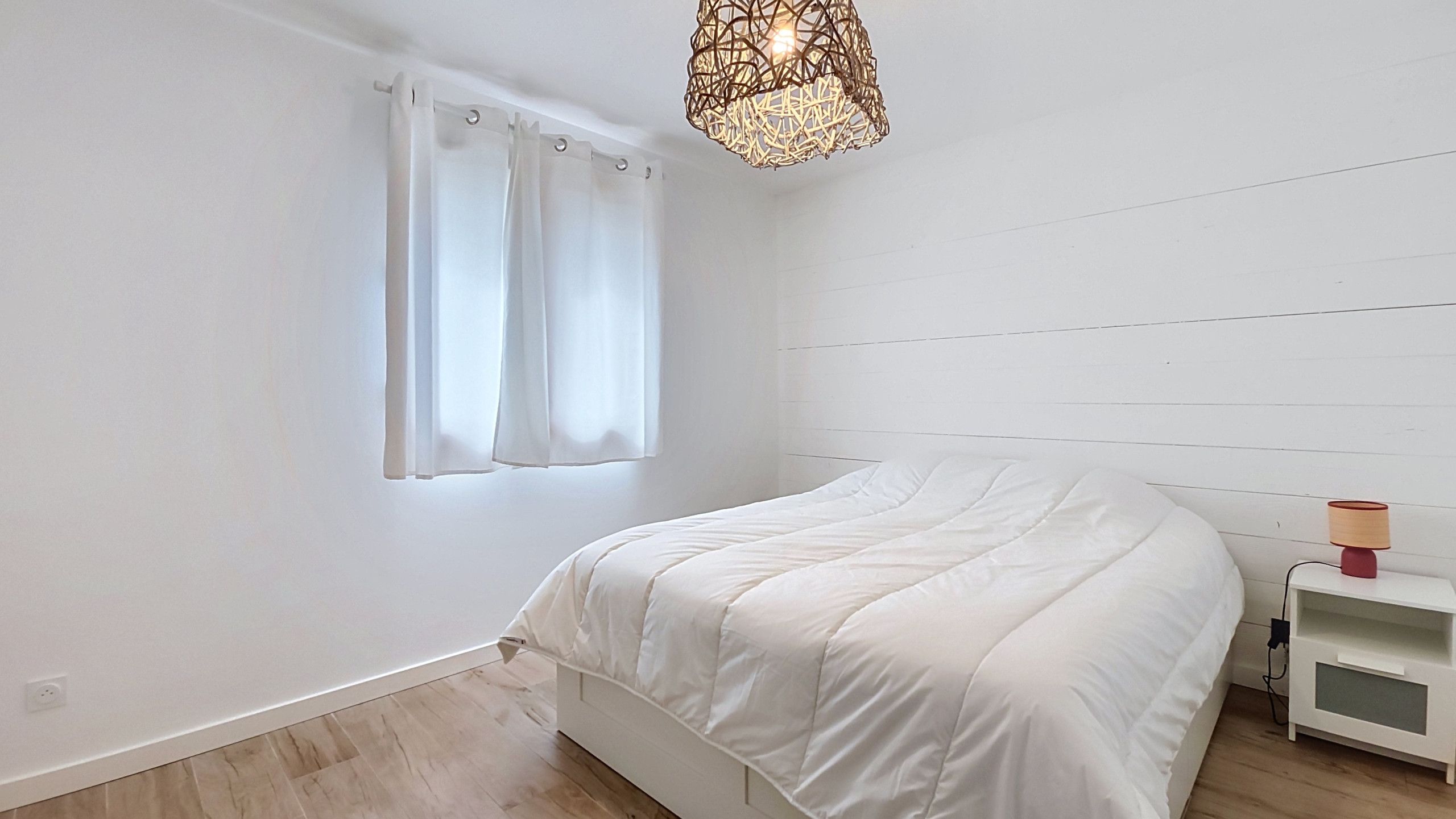 A bedroom with a bed, a nightstand, a lamp, and a window with curtains.