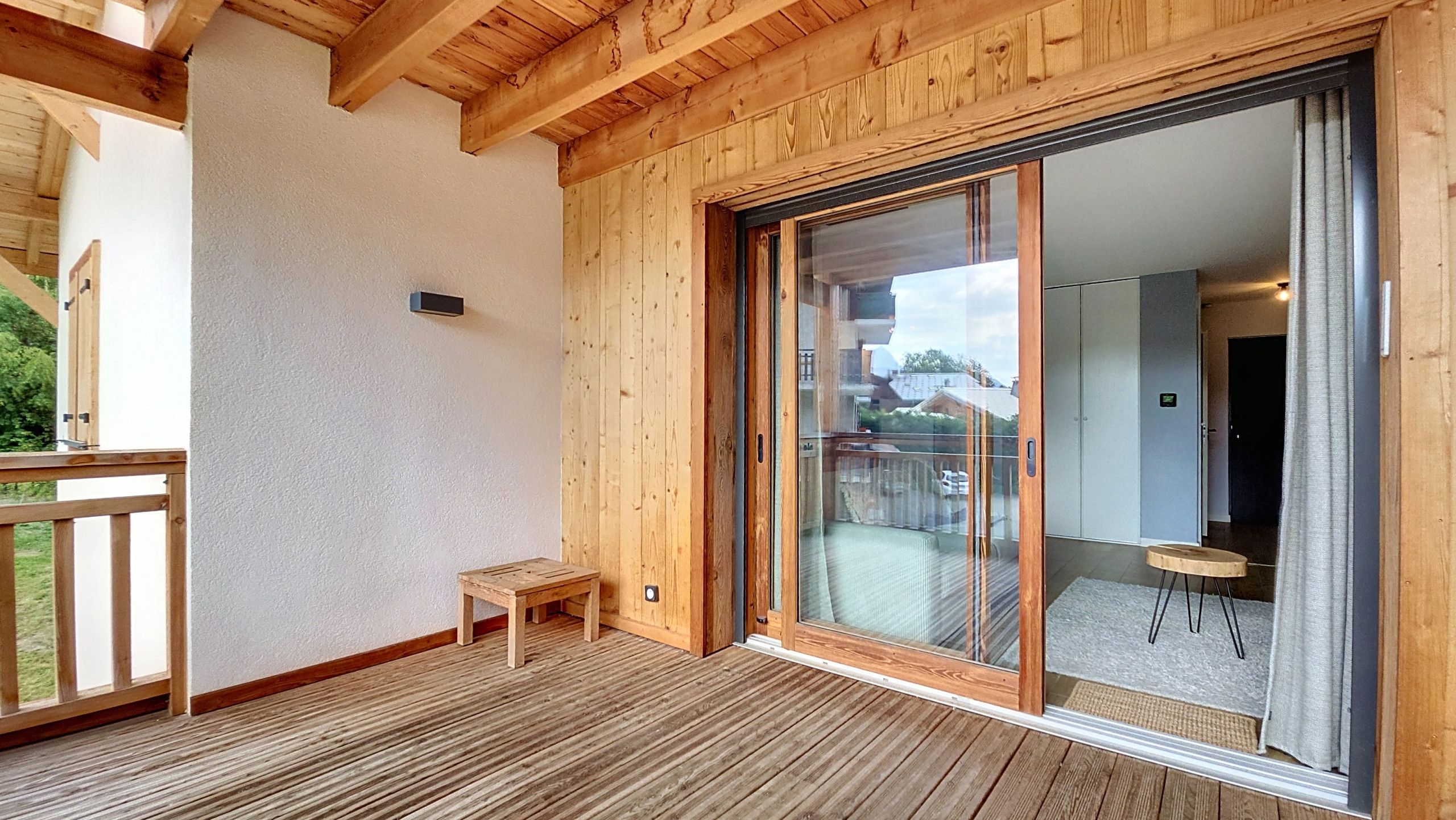 Una terraza de madera con una pequeña mesa y una puerta corrediza de vidrio que da a un espacio interior.