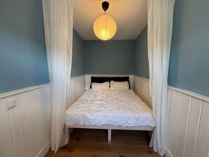 Ein Schlafzimmer mit einem Bett, weißen Vorhängen, einer Pendelleuchte und Holzböden.
