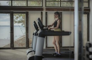 Una persona usando una cinta de correr en una habitación con ventanas amplias con vistas a la playa.