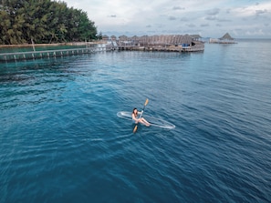A person kayaking on a calm body of water with overwater bungalows in the background.