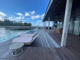 A wooden deck with lounge chairs and a small pool, overlooking a body of water and a distant island.