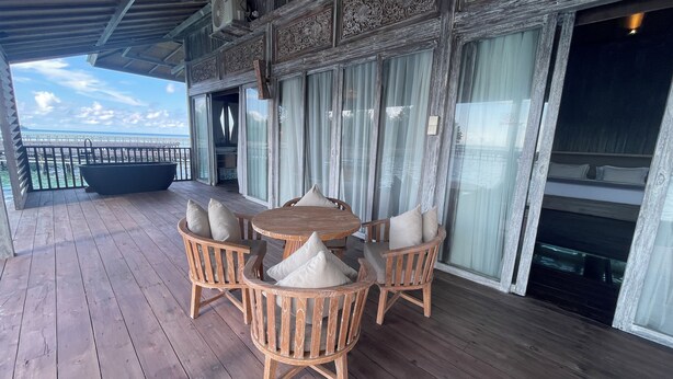 Una terraza de madera con una mesa redonda y sillas, con vista a un cuerpo de agua.