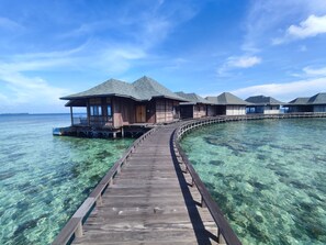 A wooden overwater bungalow with a covered walkway leading to it, set in clear turquoise waters. - Grand Mega Diving Resort Karimunjawa (Kabupaten Jepara)