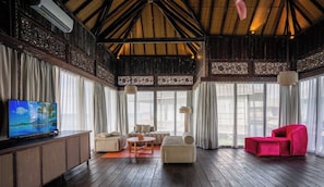 A spacious room with a wooden ceiling, a television on a cabinet, and a red chair.