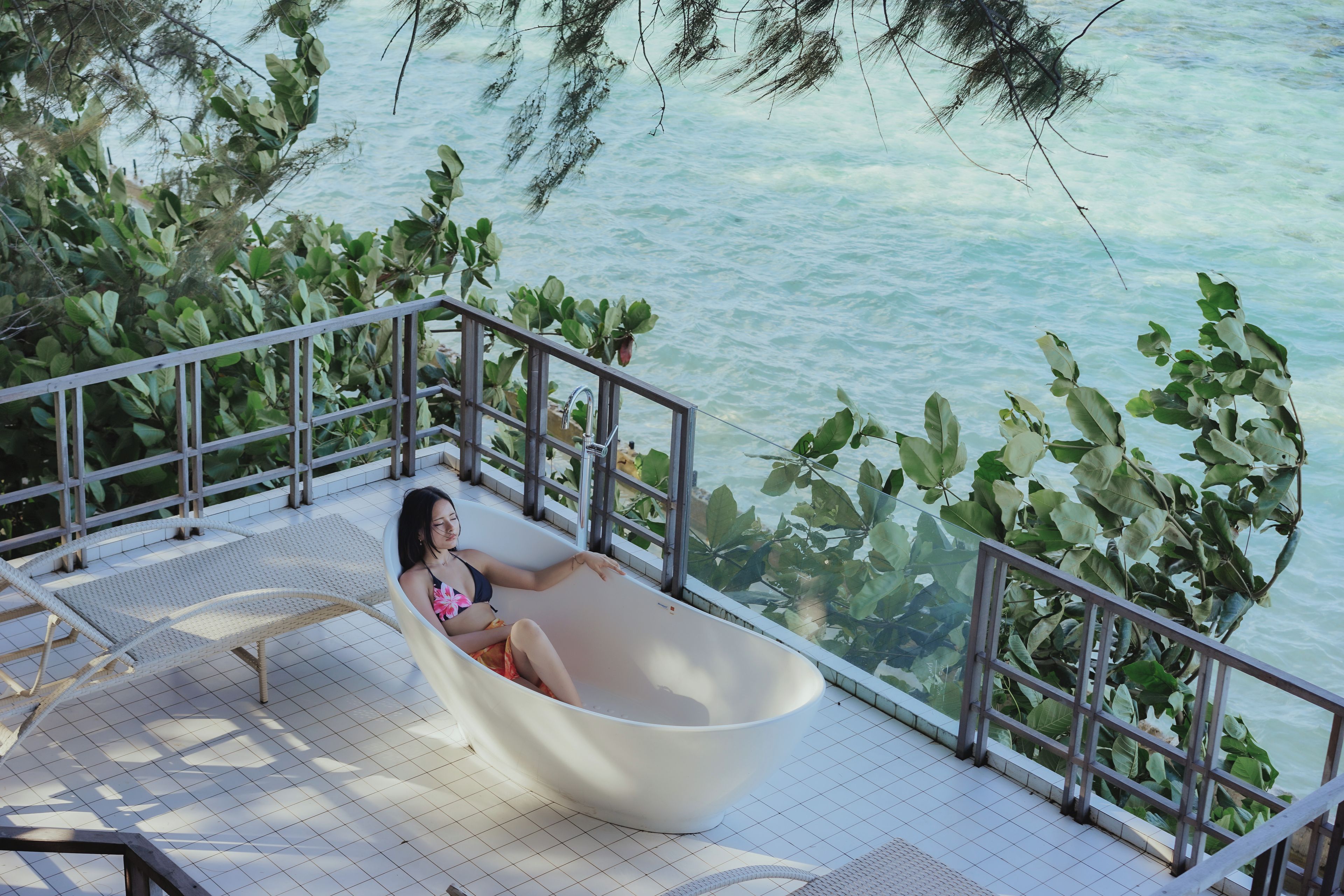 A person relaxing in a bathtub on a balcony with a view of the sea.