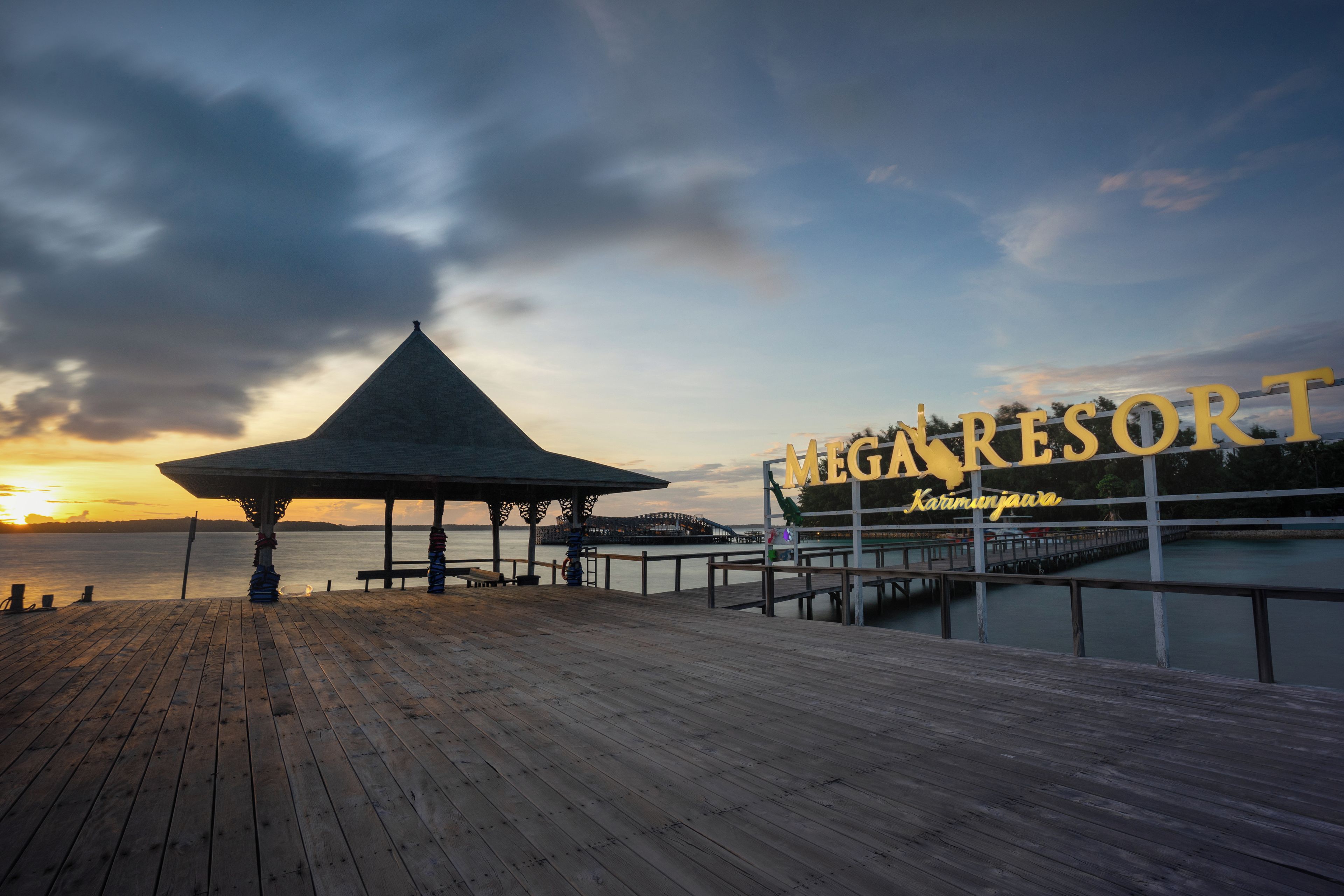 A wooden pier leading to a gazebo with a view of the sunset over water.