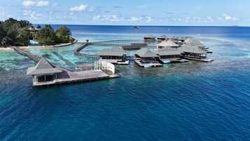 Overwater bungalows with a pier, clear turquoise water, and a distant island.