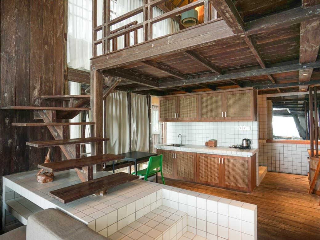 A rustic kitchen with wooden beams, a tiled backsplash, and a green chair.