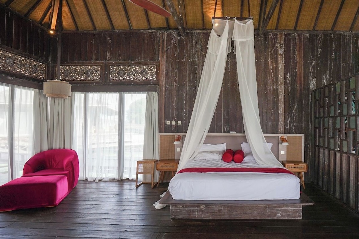 A room with a bed, a red chair, and a wooden floor.