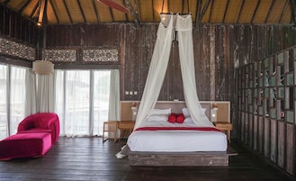 Una habitación con una cama, una silla roja y suelo de madera.