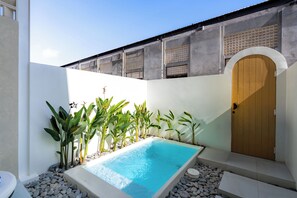 A swimming pool with a wooden door and a white wall with a window. - Villa Naya by Betterplace (Pecatu)