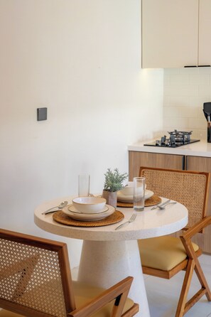A round dining table with a white top, surrounded by two wooden chairs with woven seats. - Villa Naya by Betterplace (Pecatu)