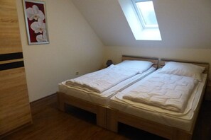 Ein Schlafzimmer mit zwei Einzelbetten, einem Oberlicht, Holzboden und einem an der Wand hängenden Bild.