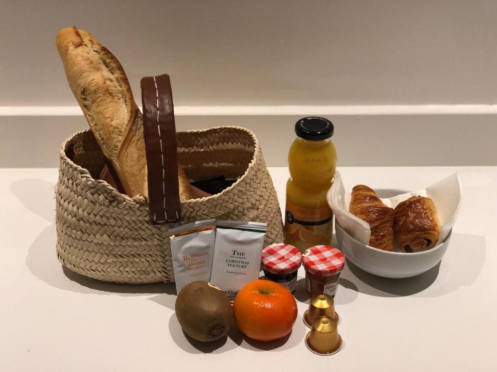 Een mand met brood, een fles, een schaal croissants, een kiwi, een sinaasappel en een theezakje.