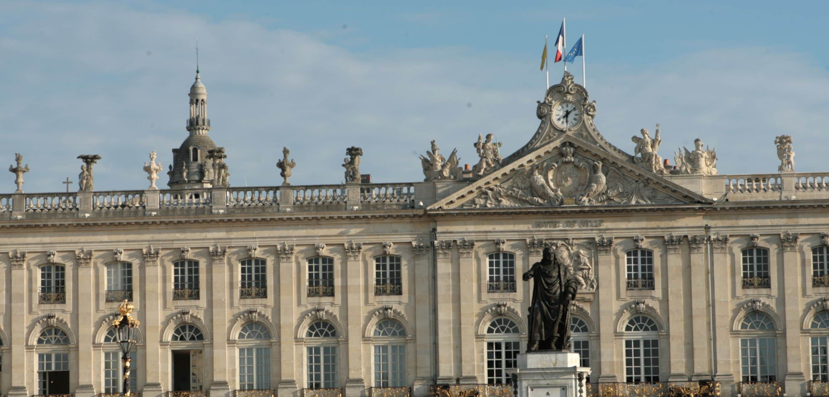 Un imposant bâtiment historique à l’architecture classique, caractérisé par un beffroi remarquable, des statues et une façade symétrique.