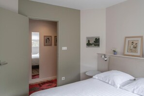 A bedroom with a bed, a bedside table, a wall-mounted light, and a door leading to another room.