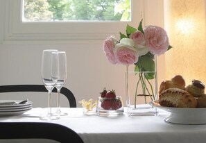 A dining table with a vase of flowers, a glass of water, a plate of strawberries, and a plate of pastries. - Les Suites de Catherine, la si Calme (Nancy)