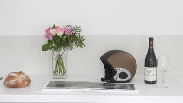 A white counter with a vase of pink flowers, a helmet, a bottle of wine, and a glass.