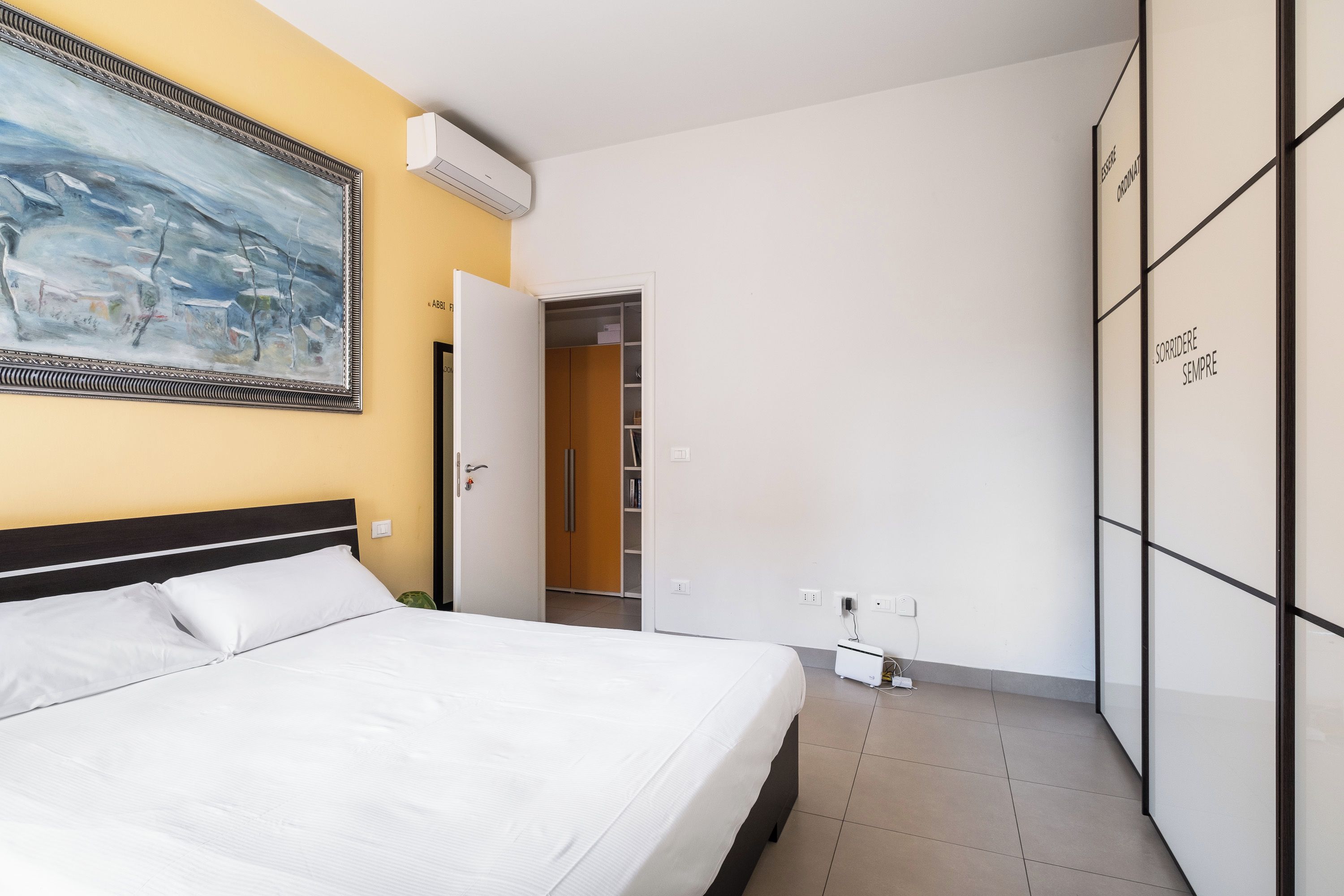 Quarto de hotel com cama, guarda-roupa, um quadro na parede e ar condicionado.