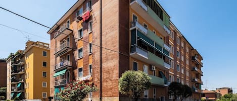 A multi-story residential building with balconies, a gated parking area, and a clear blue sky.