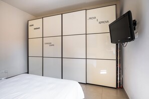 A bedroom with a bed, a wardrobe with compartments labeled 'ESSERE ORDINATI,' 'PROVA E RIPROVA,' and 'SORRIDER E SEMPRE.' A flat-screen TV is mounted on the wall. - Bergonzoni Modern Apartment by Wonderful Italy (Bologna)