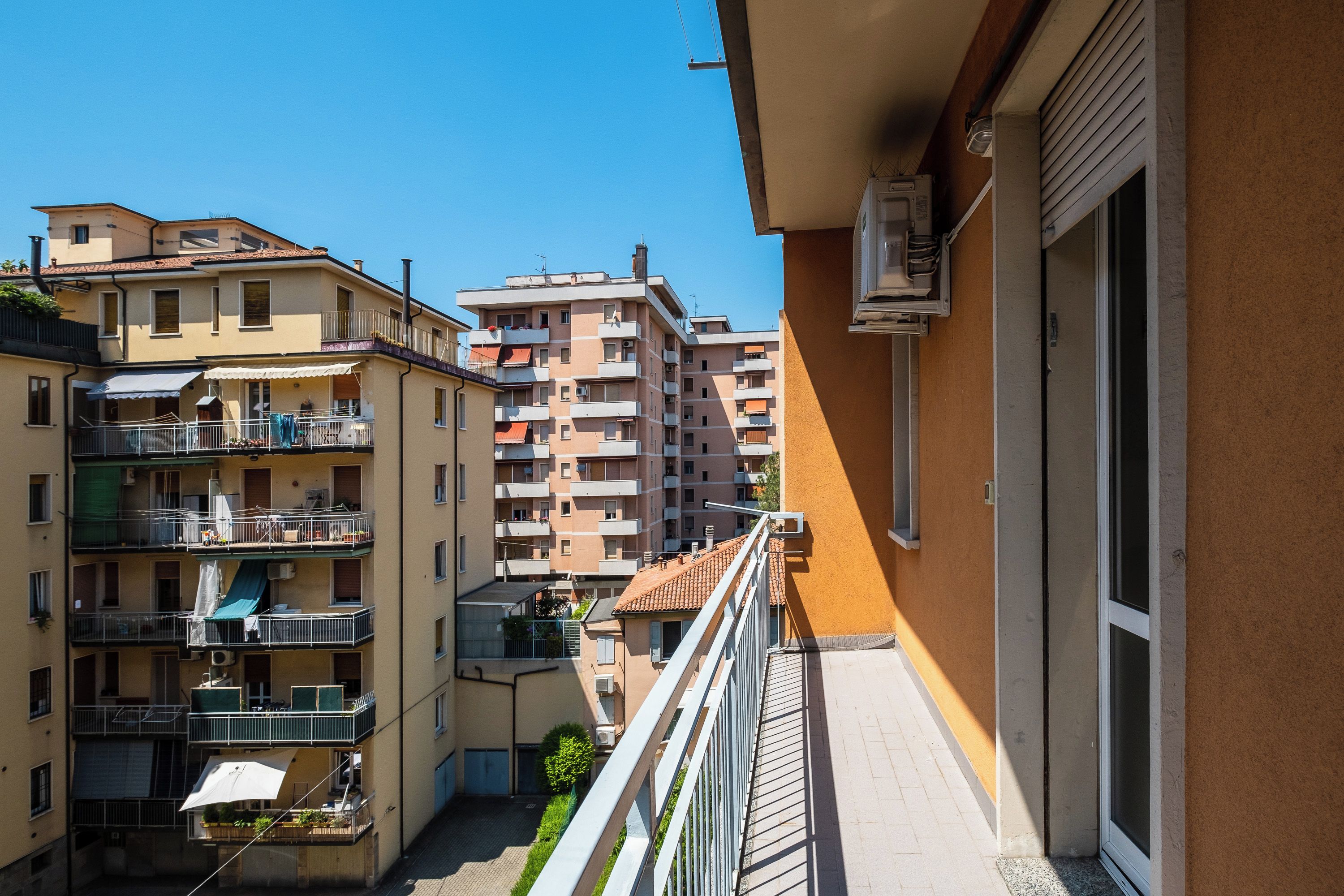 Edifício residencial com várias sacadas, céu claro e vista para edifícios vizinhos.