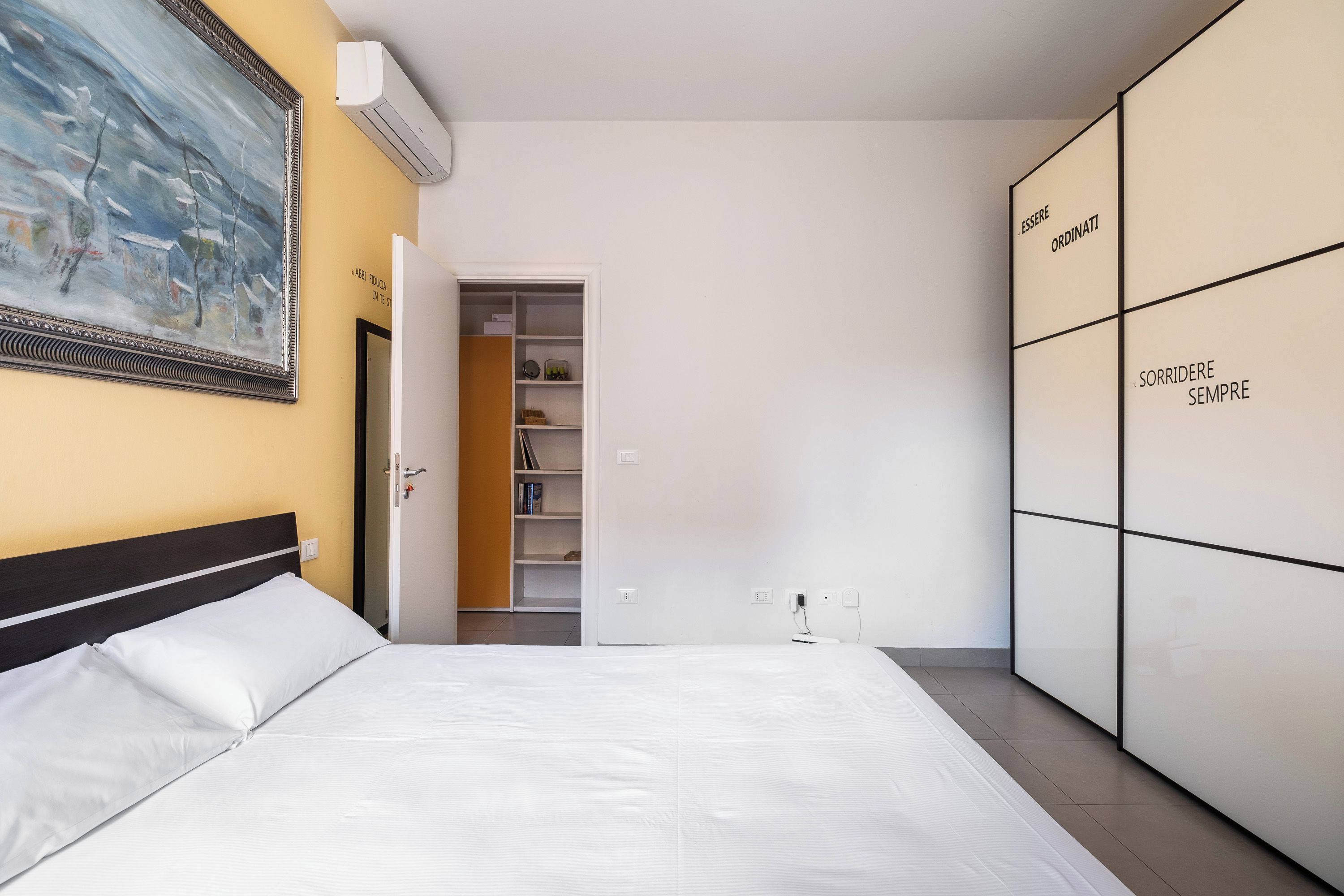 A bedroom with a bed, a wardrobe, a painting, and a door leading to a closet.
