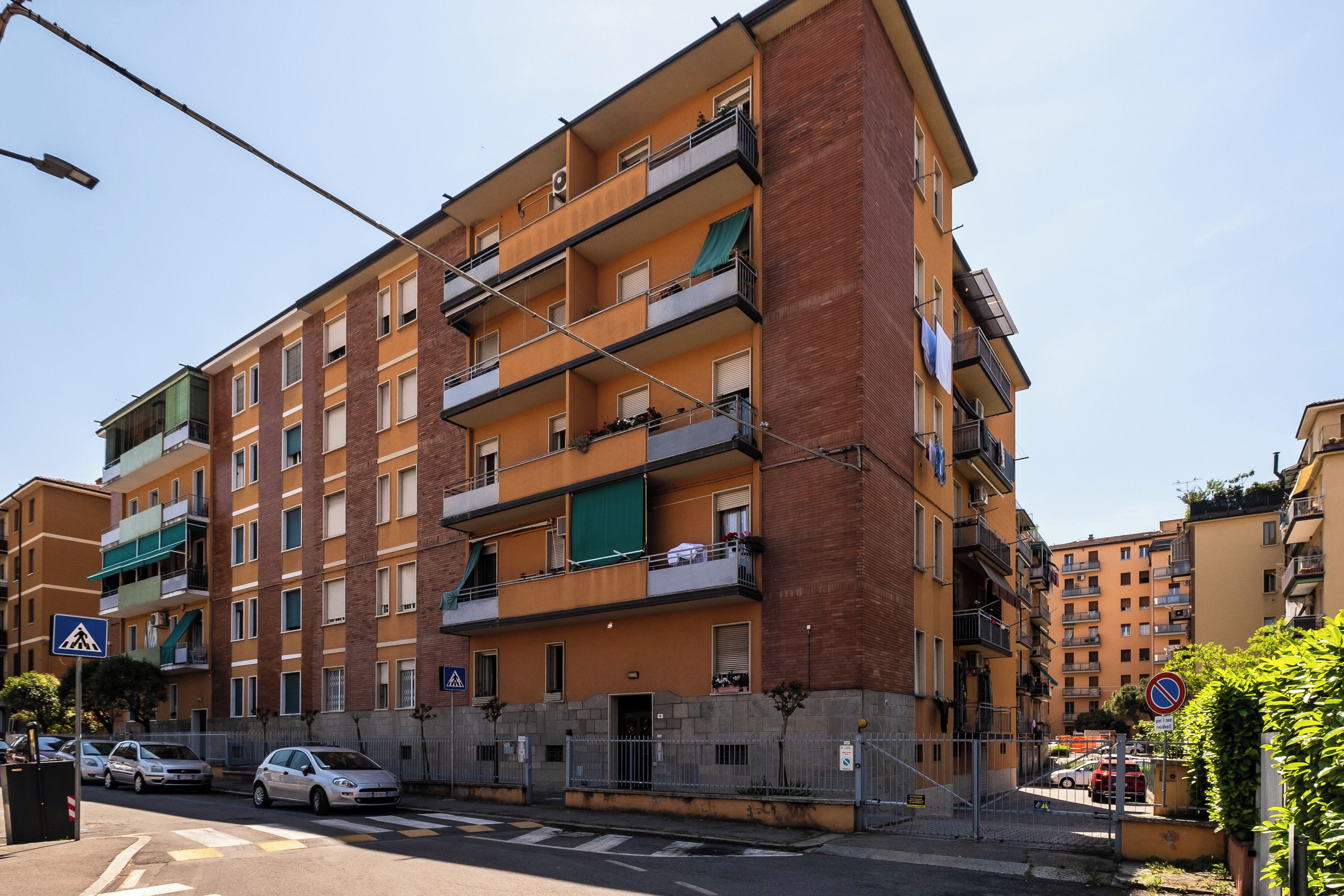 A multi-story residential building with balconies, a pedestrian crossing, and a no parking sign.