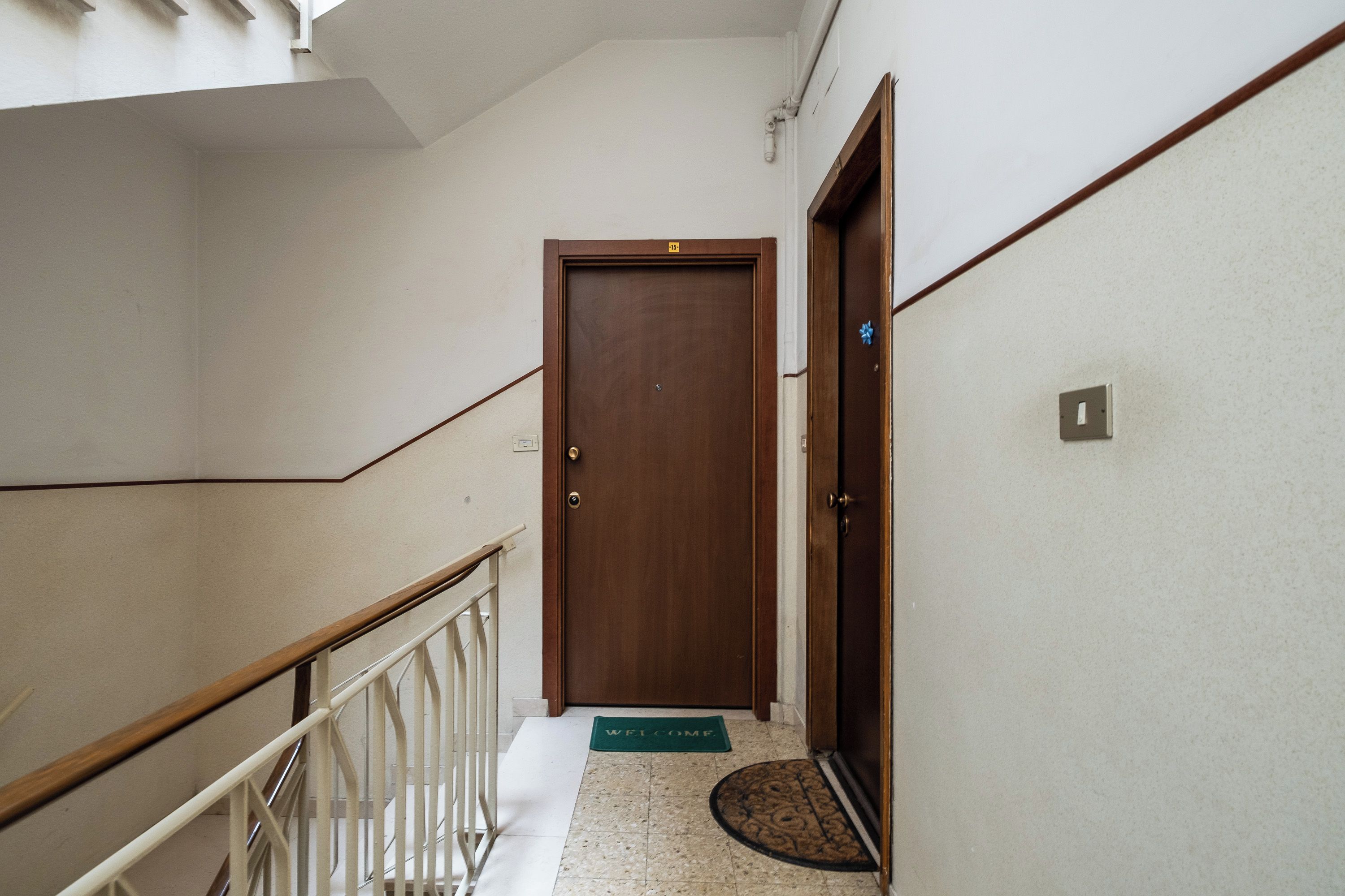 A hallway with a wooden door, a white railing, and a welcome mat.