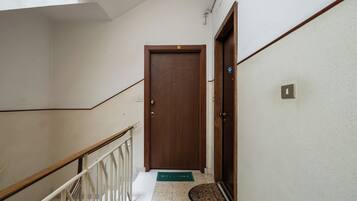 A hallway with a wooden door, a white railing, and a welcome mat.