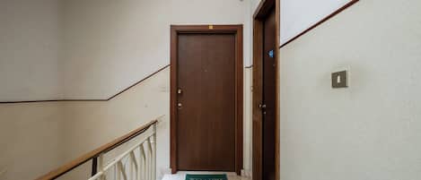A hallway with a wooden door, a white railing, and a welcome mat.