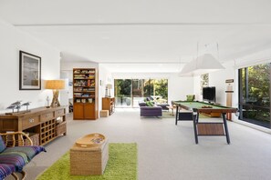 A modern living room with a pool table, a bookshelf, a sofa, and a large window offering a view of the outdoors. - Ocean View House Fairhaven (Fairhaven)
