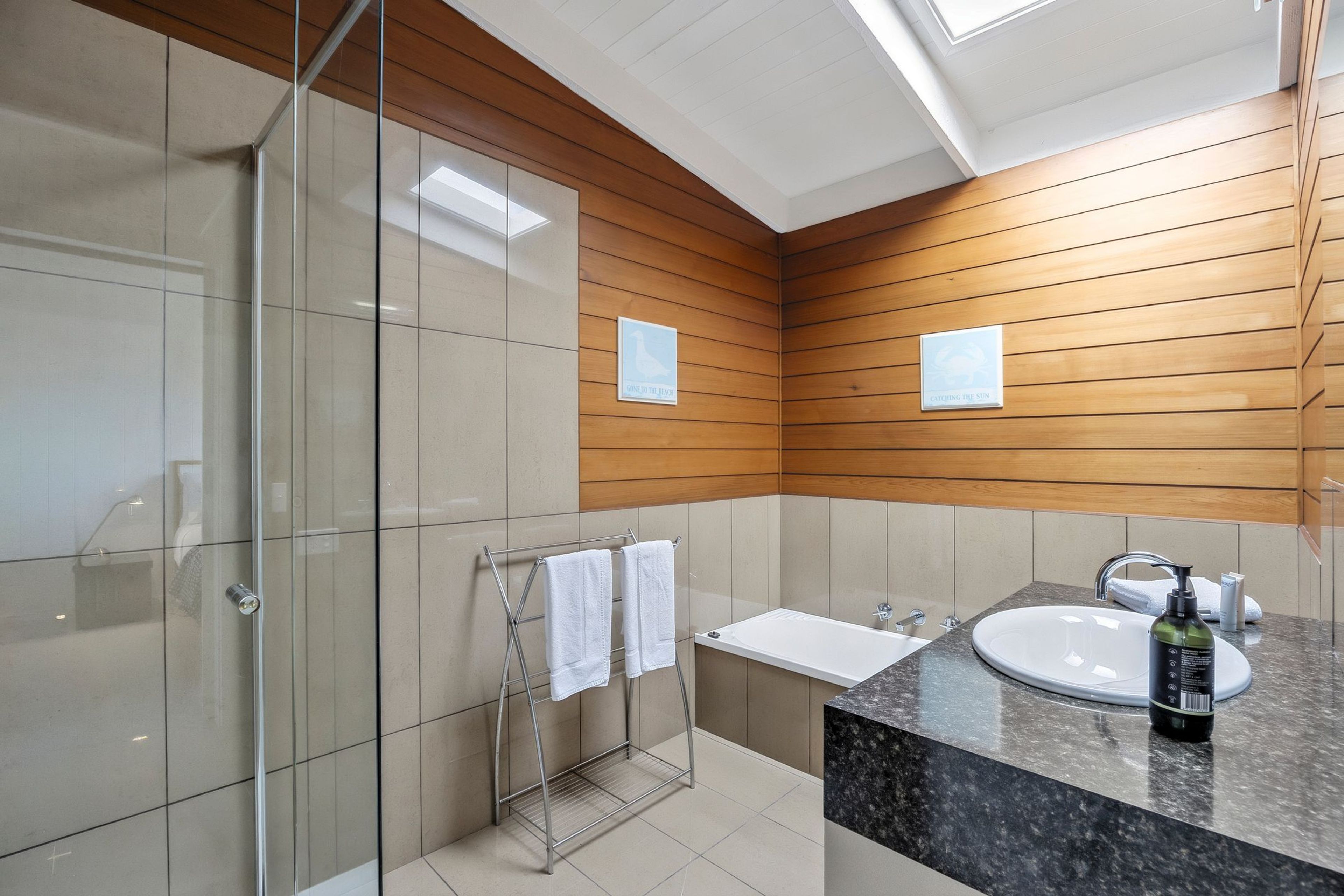 Un baño moderno con cabina de ducha de vidrio, panel de pared de madera, lavamanos blanco y encimera de mármol.