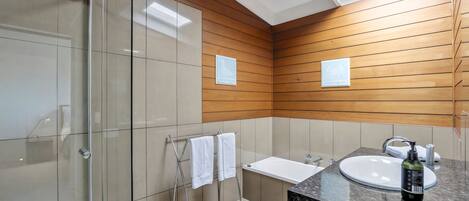 Un baño moderno con cabina de ducha de vidrio, panel de pared de madera, lavamanos blanco y encimera de mármol.