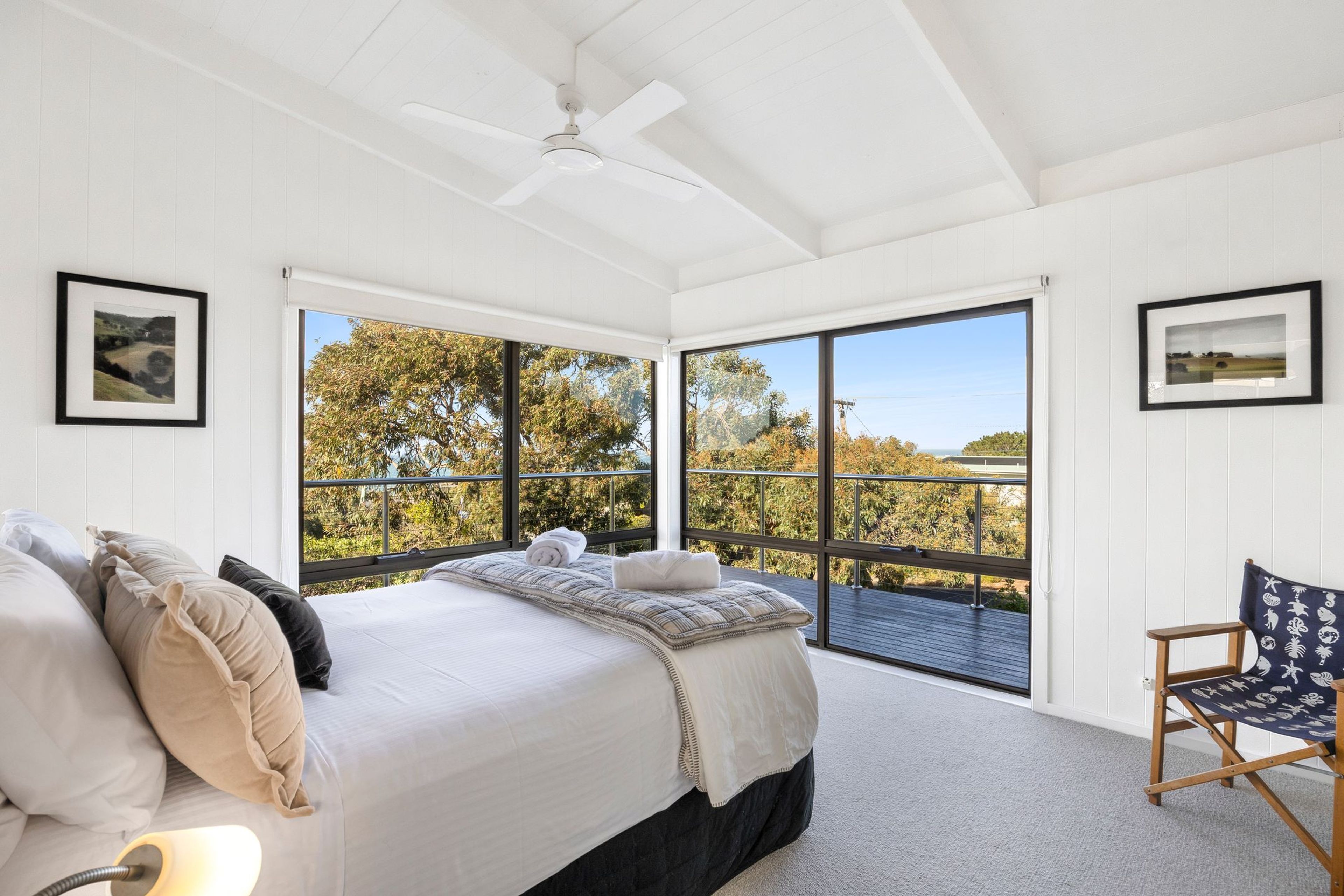 A bedroom with a large bed, a chair, and a view of trees through floor-to-ceiling windows.