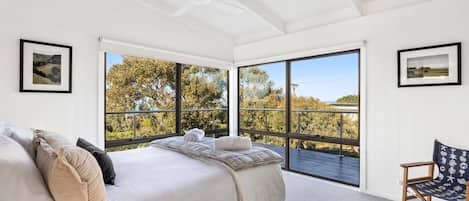 Un dormitorio con una cama grande, una silla y vistas a árboles a través de ventanales del suelo al techo.