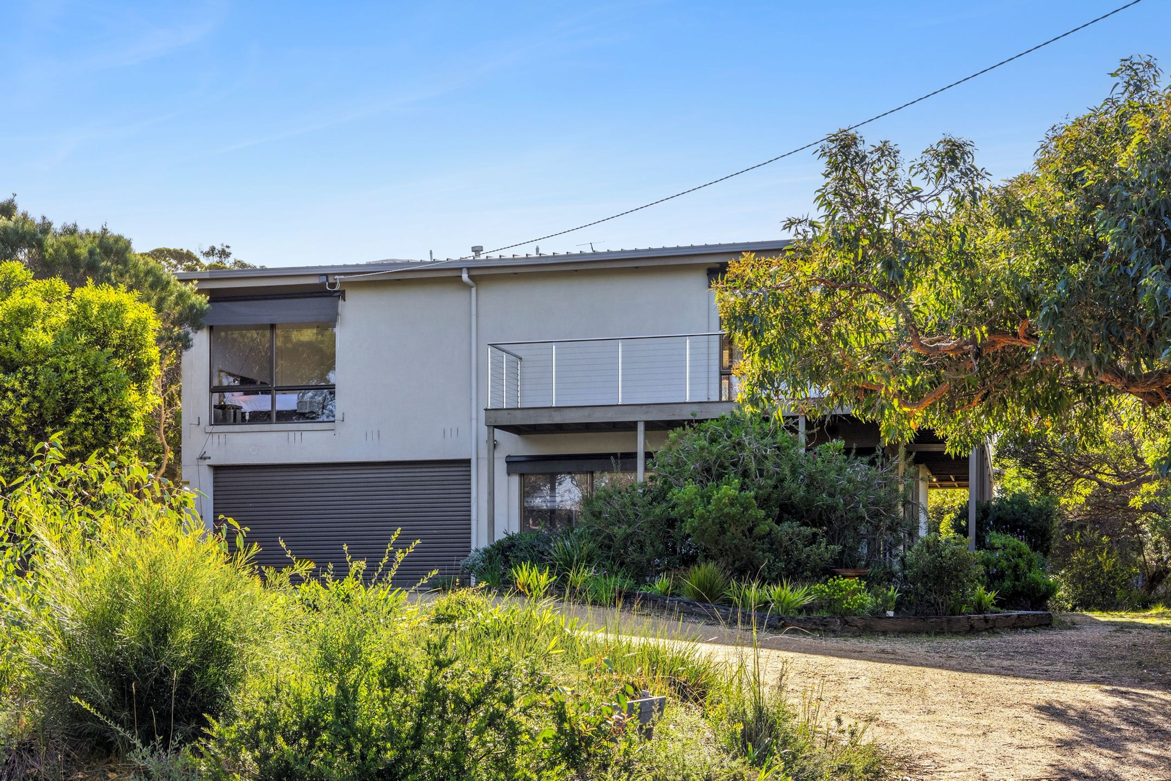 A modern two-story house with a garage, surrounded by lush greenery and trees.