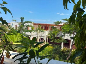 A courtyard with a building featuring arched windows and a red roof, surrounded by lush greenery. - Waridi North | Breeze – 2BR Upper Floor (Diani Beach)