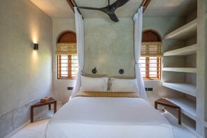 A bedroom with a large bed, two bedside tables, a ceiling fan, and a window with a view. - Waridi North | Breeze – 2BR Upper Floor (Diani Beach)