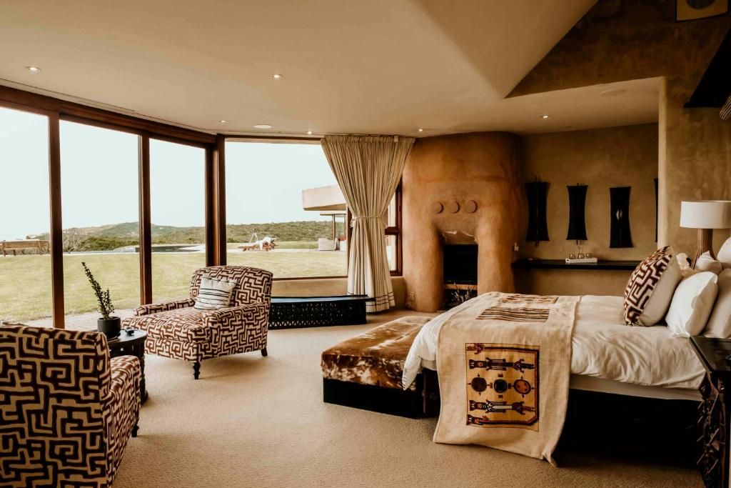 A bedroom with a large window, a bed, a chair, and a fireplace.