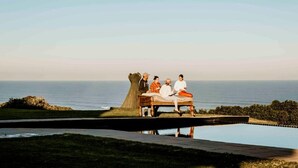 A group of people sitting on a bench overlooking a body of water with a clear sky.