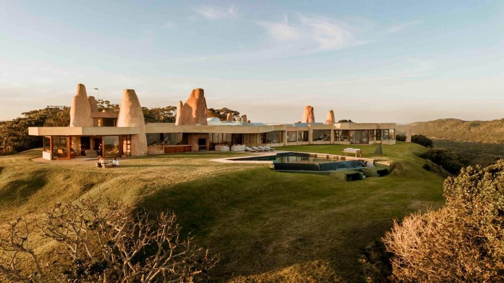 A modern house with a unique architectural design featuring multiple conical structures, a spacious lawn, and a swimming pool.