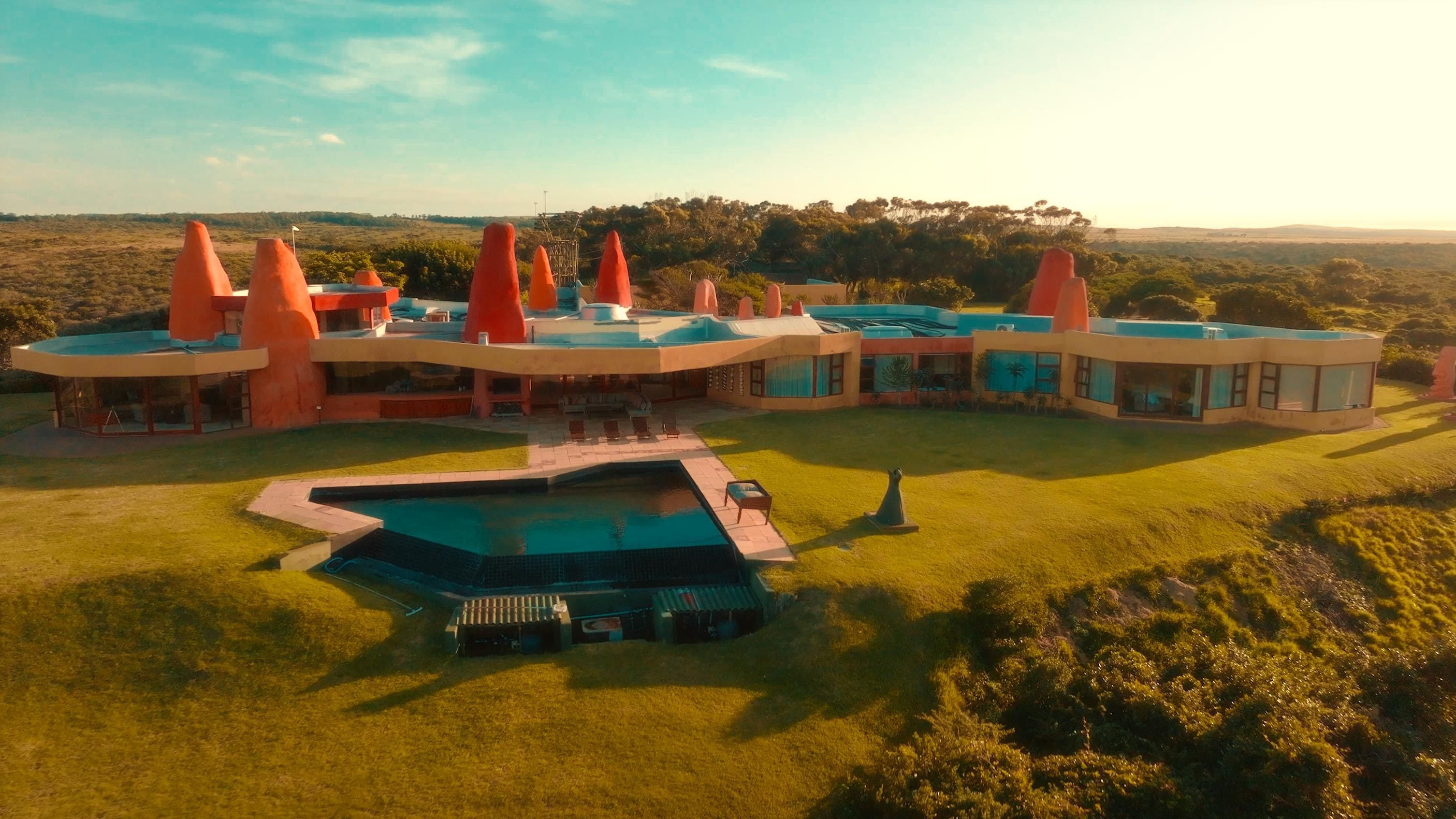 A modern villa with a swimming pool, multiple dining areas, and a large lawn.